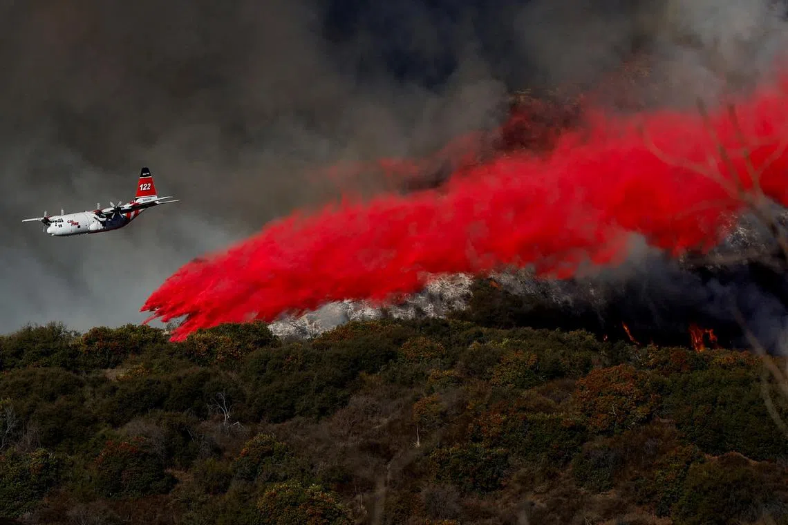 A plane makes a drop as smoke billows from the Palisades Fire at the Mandeville Canyon, in Los Angeles on Jan 11.