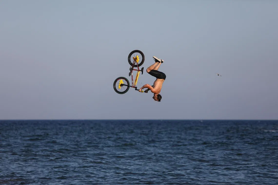 epa11489646 A bmxer rides his bike over a ramp that was set up by the sea and dives into the water, during a small event that was organized by Gutlessbmx Crew, celebrating the world BMX Day, in Mati on the east coast of the Attica region, Greece, 20 July, 2024.  EPA-EFE/GEORGE VITSARAS