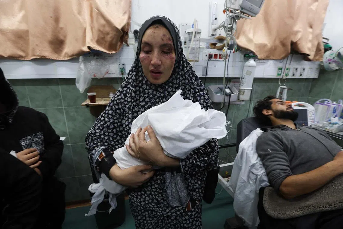 Mother of two Palestinian children, a newborn Al-Amera Ayesha and a young boy Ahmed Zourob, who were killed in an Israeli strike, amid the ongoing conflict between Israel and the Palestinian Islamist group Hamas, holds her child next its wounded father, in Rafah, in the southern Gaza Strip, December 19, 2023. REUTERS/Ibraheem Abu Mustafa
