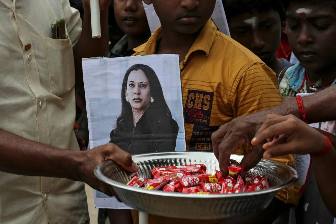A man holds a placard with the photo of U.S. Vice President-elect Kamala Harris as another distributes sweets during the celebration on the day of her inauguration, in the village of Thulasendrapuram, where Harris' maternal grandfather was born and grew up, in the southern Indian state of Tamil Nadu, India, January 20, 2021. 