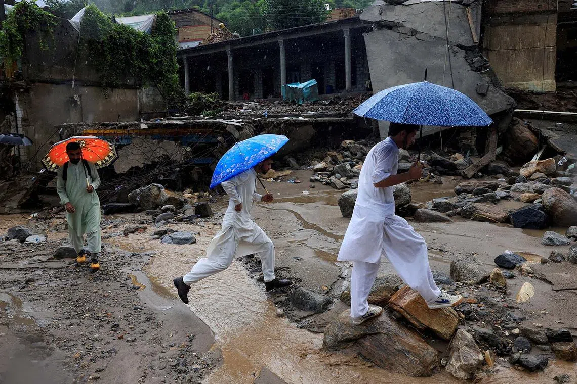 Volunteers walking with umbrellas as they survey the damage caused by a storm that caused heavy rains and flooding in Bayshonai Kalay, Pakistan, Aug 18, 2025. 