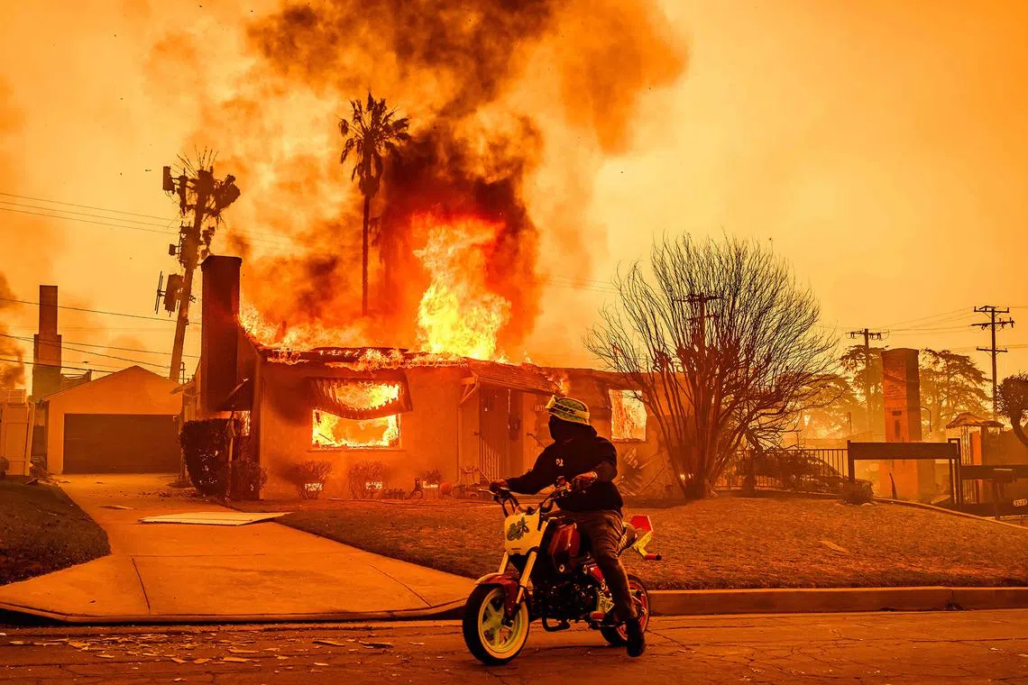 A motorcyclist stopping to look at a burning home during the Eaton fire in the Altadena area of Los Angeles county, California on Jan 8, 2025. At least five people are now known to have died in wildfires raging around Los Angeles, with more deaths feared.