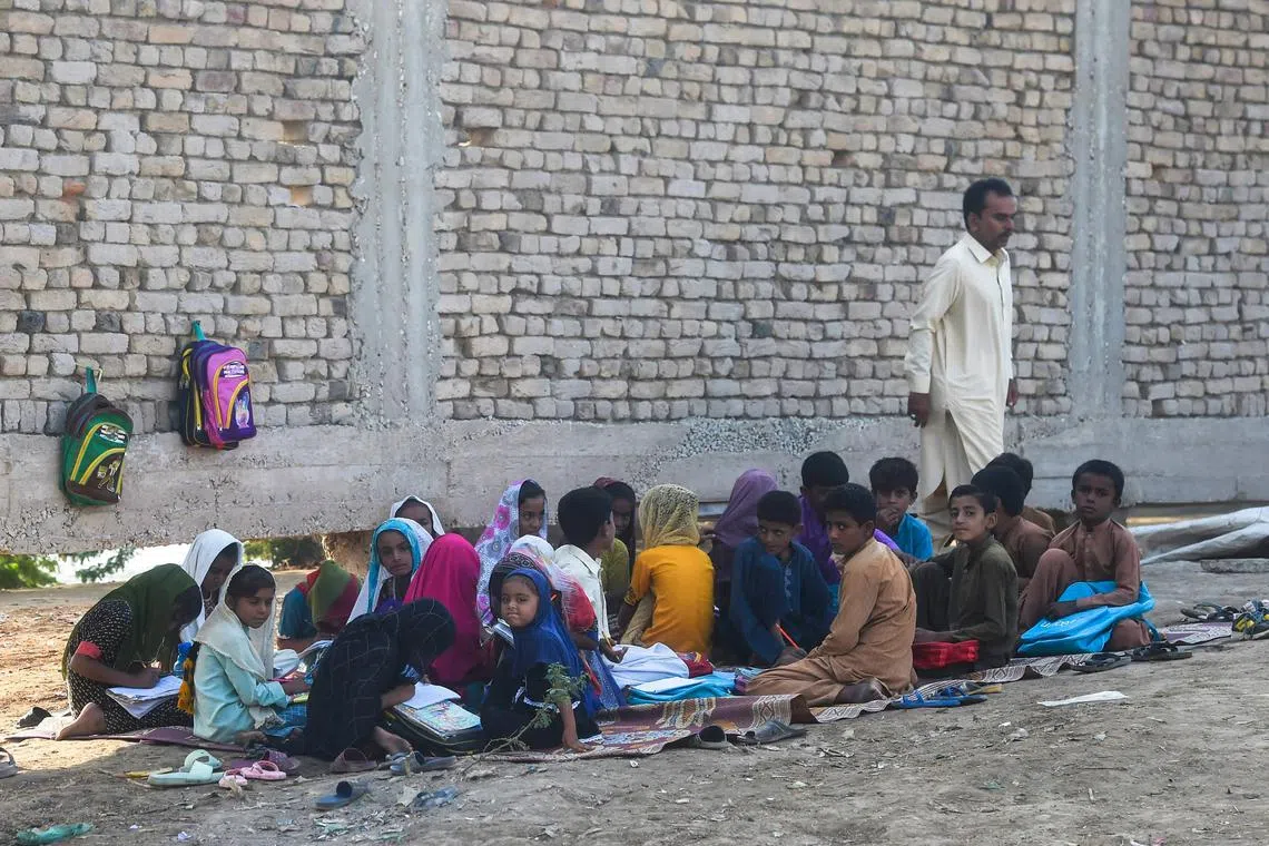 Students attend school as they sit outside their flood-affected classroom in Chandan Mori, Sindh, on Oct 28, 2022.