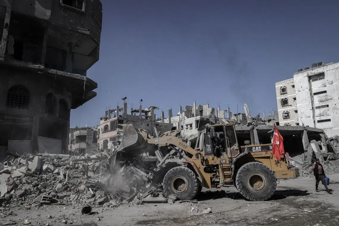 A bulldozer carrying a Turkish flag clears rubble between destroyed buildings in Gaza City, Gaza, on Tuesday, Oct. 21, 2025. US Vice President JD Vance said he remains optimistic about the future of a ceasefire between Israel and Hamas despite a flareup in violence over the weekend, part of a bid to keep talks progressing on the future of Gaza. Photographer: Ahmad Salem/Bloomberg