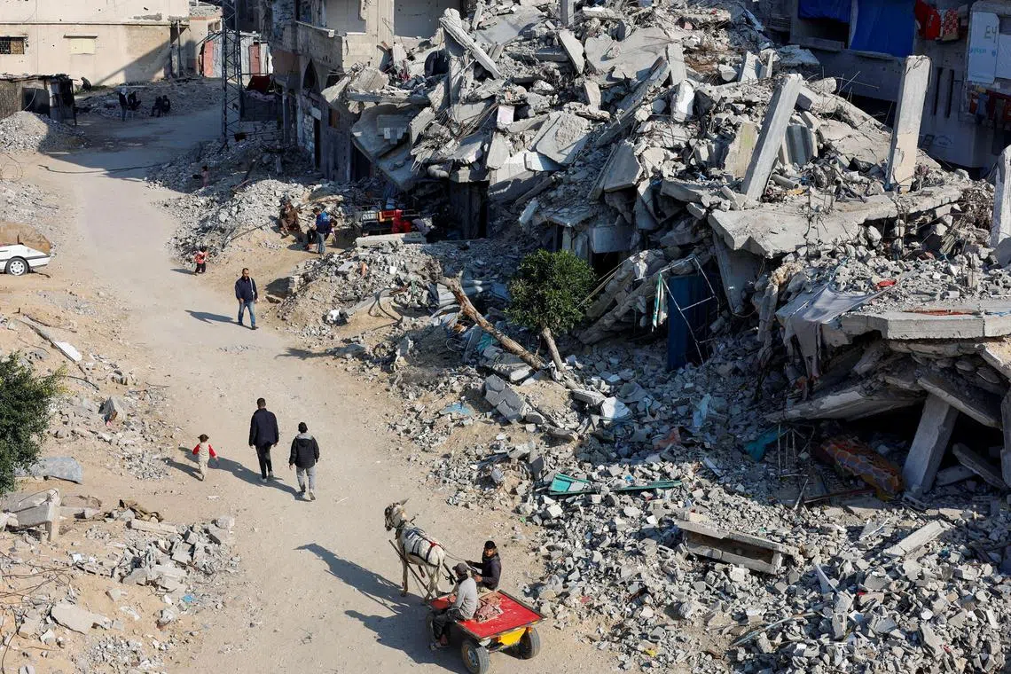 Palestinians ride a donkey-drawn cart as others walk past the rubble of houses in Khan Younis, southern Gaza Strip.