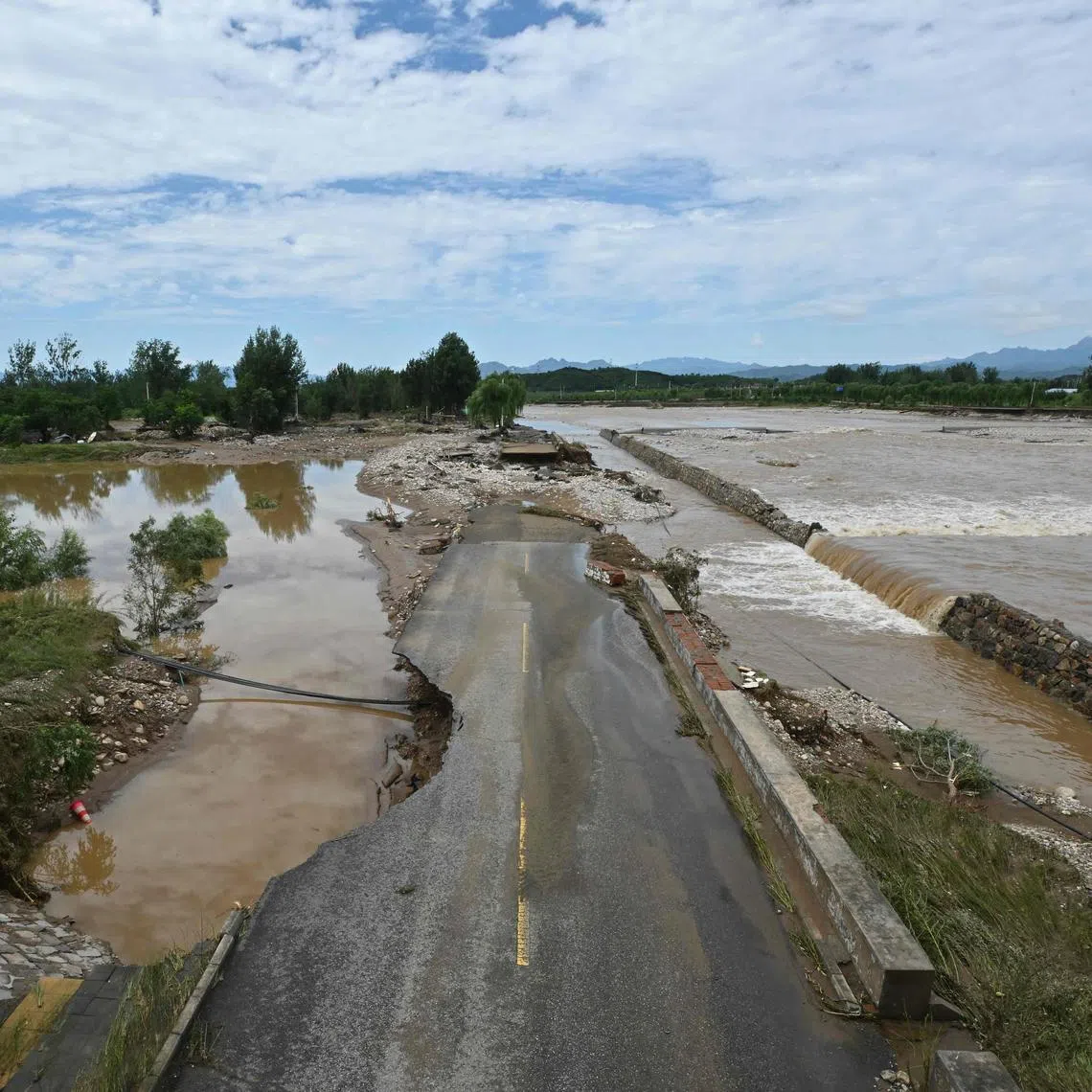 A flood-damaged road is seen alongside a swollen river following heavy rains in Miyun district, on the outskirts of Beijing, on July 29. 