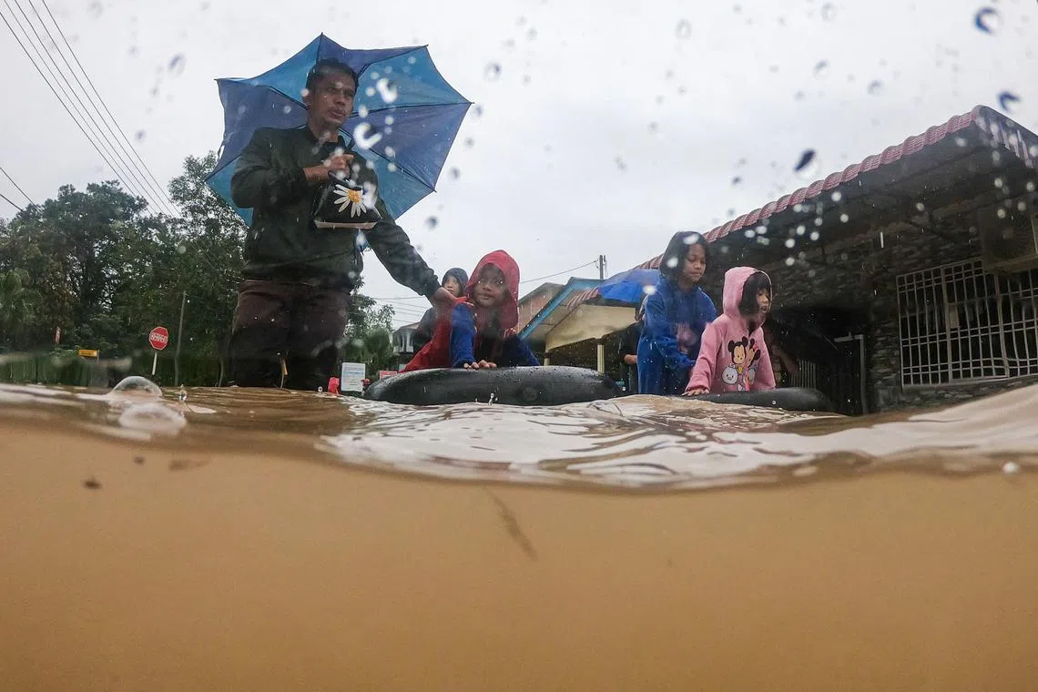 A family wade through floodwaters after evacuating their home in a flooded area in Yong Peng, Malaysia's Johor state on March 4, 2023. 