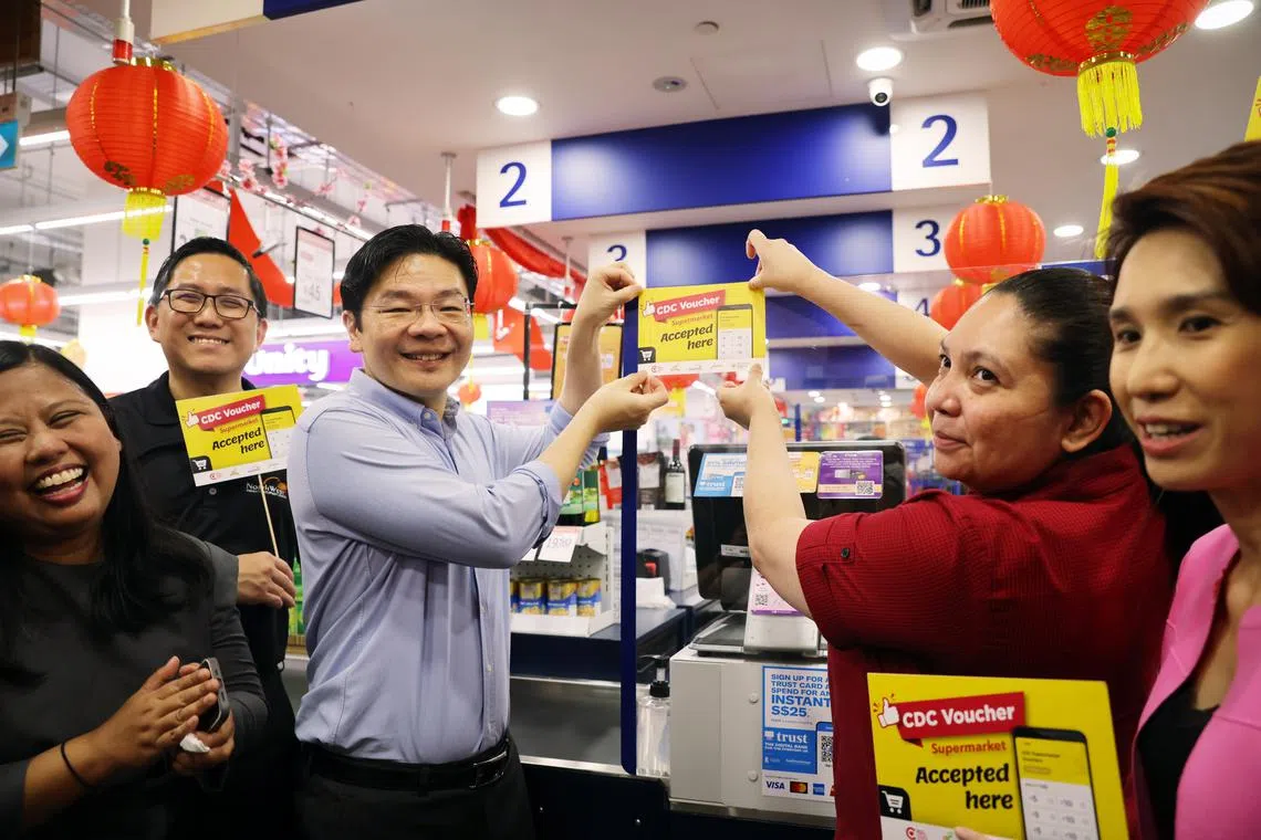 Deputy Prime Minister Lawrence Wong and FairPrice cashier Nur Alisha putting up a CDC voucher decal at a FairPrice outlet in Kampong Admiralty on Tuesday.
