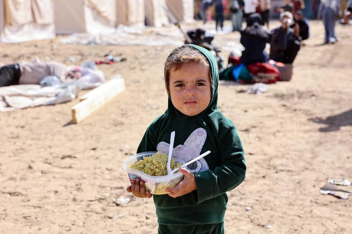 A displaced Palestinian child - who fled the northern Gaza Strip with family members due to Israeli army operations - carrying a bowl of food in front of newly set up tents at a former football arena in Gaza City, on Oct 25.