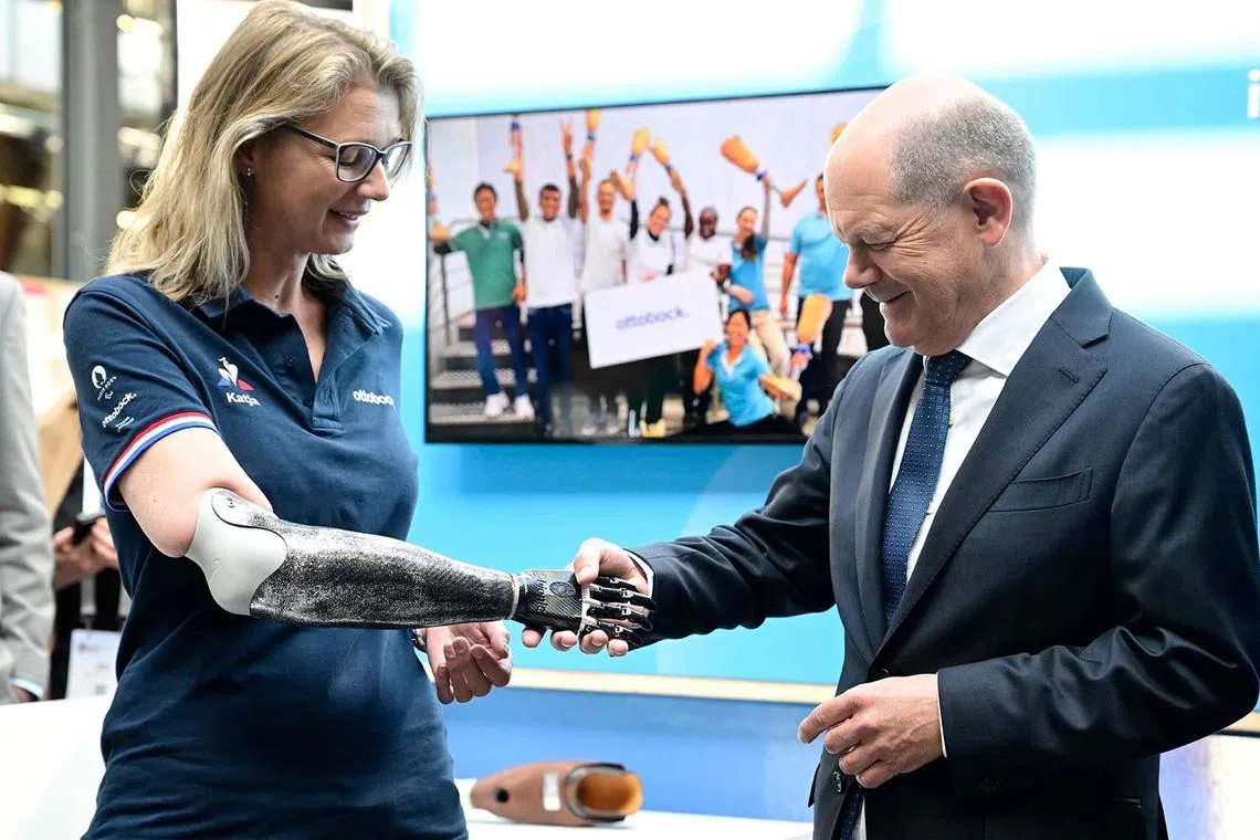 TOPSHOT - German Chancellor Olaf Scholz (R) shakes hands with the prosthetic hand of a worker of the German med-tech company Ottobock during the opening of the Global Disability Summit in Berlin, on April 2, 2025. The third Global Disability Summit (GDS) is held from April 2 to April 3, 2025 in Berlin, Germany, hosted by the International Disability Aliance, the Government of Germany and the Government of Jordan. (Photo by John MACDOUGALL / AFP)