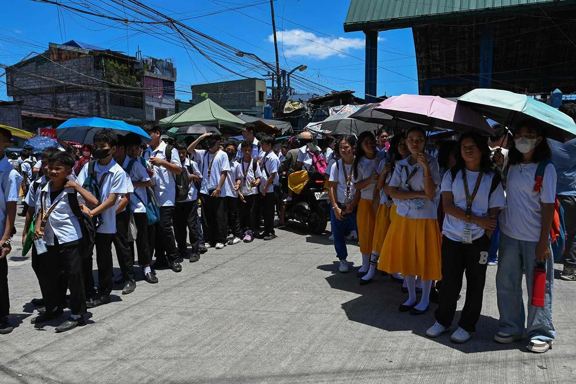 Students use umbrellas to protect themselves from the sun as they line up to wait for their classes outside their school in Manila on April 2, 2024. More than a hundred schools in the Philippine capital shut their classrooms on April 2, as the tropical heat hit "danger" levels, education officials said. 