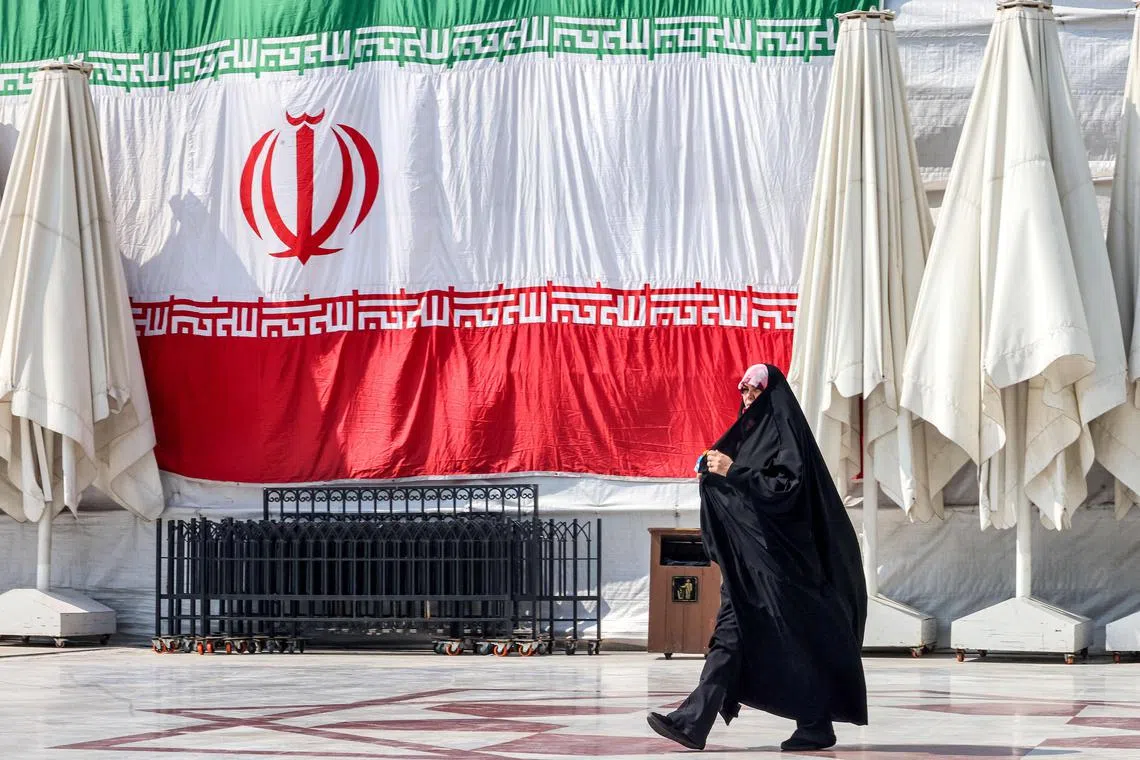 A woman walks past a giant Iranian national flag hanging outside at the Emamzadeh Saleh mosque in Tajrish square in northern Tehran on March 12, 2024, on the first day of the holy fasting month of Ramadan in the Islamic Republic. (Photo by ATTA KENARE / AFP)
