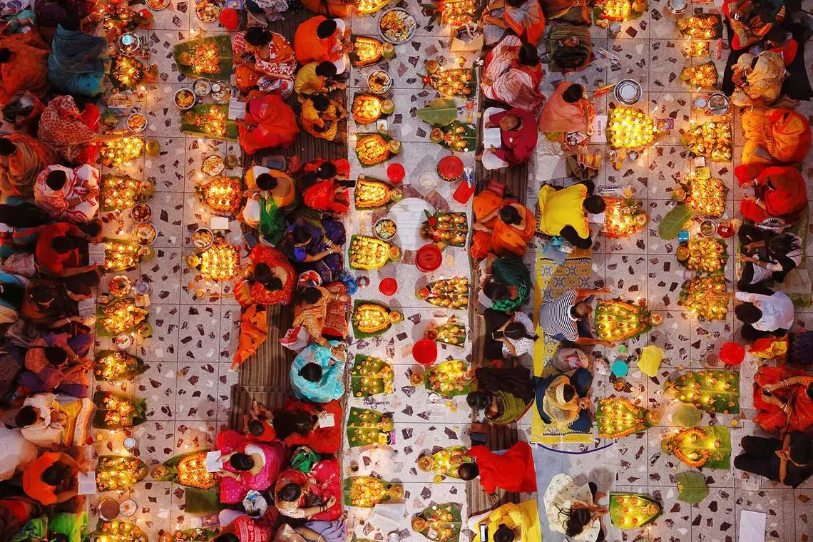 Hindu devotees sit together on the floor of a temple with oil lamps, praying to Lokenath Brahmachari, a Hindu saint, as they observe Rakher Upabash, in Dhaka, Bangladesh, Nov 5, 2022. 