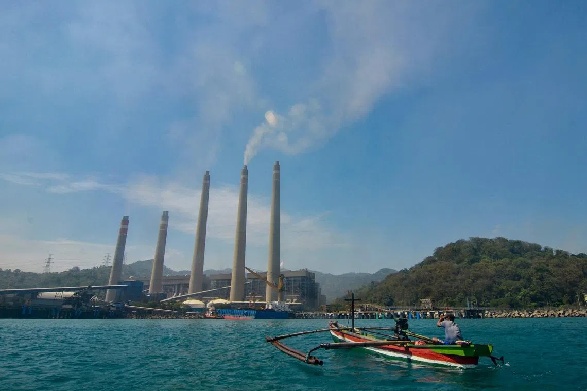 This photo taken on September 22, 2021 shows fishermen on their boat as smoke rises from chimneys at the Suralaya coal power plant in Cilegon. - Smokestacks belch noxious fumes into the air from a massive coal-fired power plant on the Indonesian coast, a stark illustration of Asia's addiction to the fossil fuel which is threatening climate targets. (Photo by RONALD SIAGIAN / AFP) / TO GO WITH Climate-UN-COP26-Asia-coal,FEATURE by Haeril Halim and Sam Reeves
