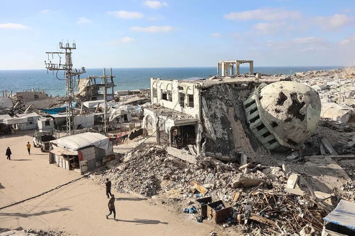TOPSHOT - Displaced Palestinians walk past destroyed buildings and makeshift shelters near the al-Shati refugee camp, west of Gaza City, on July 1, 2026. Gaza remains gripped by daily violence, with both the Israeli military and Hamas accusing one another of violating the truce in effect since October 10. The war flattened swathes of the territory, displaced most of the population at least once, and left hundreds of thousands of people living in tents and temporary shelters. (Photo by Omar AL-QATTAA / AFP)