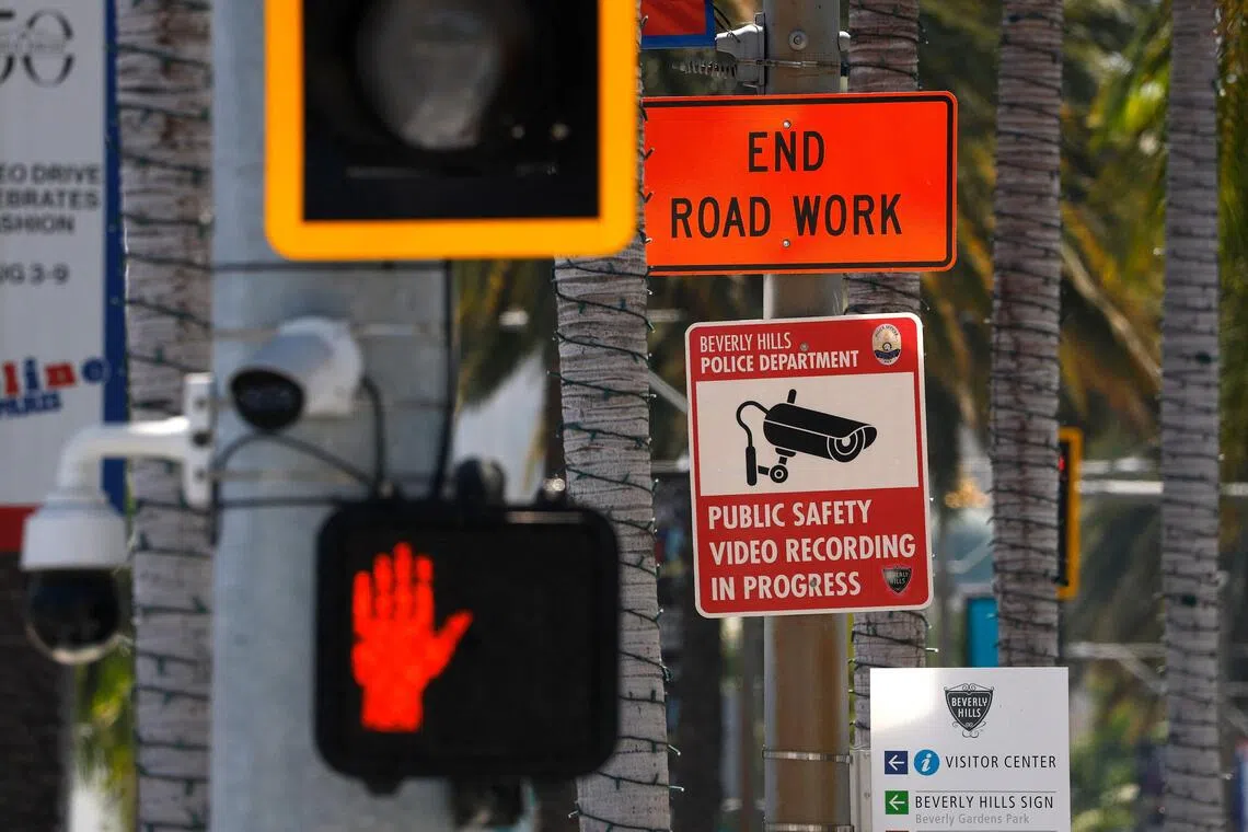 Street signs and traffic lights on a pole in an outdoor setting.