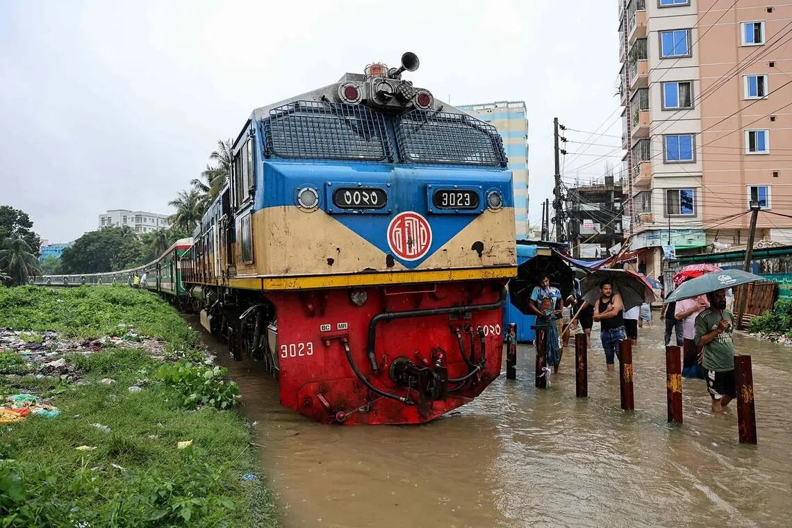 TOPSHOT - People wade through submerged railway tracks beside a stranded train following heavy monsoon rains in Chattogram on July 7, 2026. (Photo by AFP)