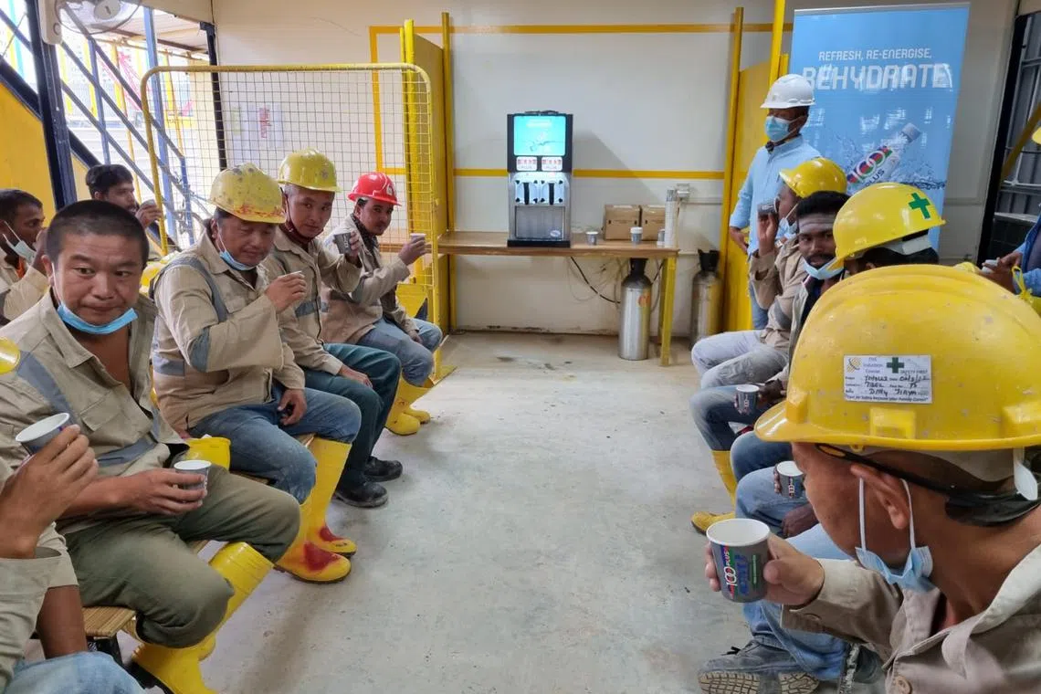 Workers at an outdoor construction site in Yishun under Teambuild Engineering and Construction having an ice slurry made from a dispenser (in background) during a break in July 2022.