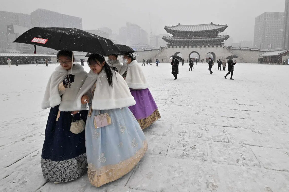 TOPSHOT - Visitors wearing traditional hanbok dress walk through Gyeongbokgung palace during snowfall in central Seoul on December 15, 2022. (Photo by Jung Yeon-je / AFP)
