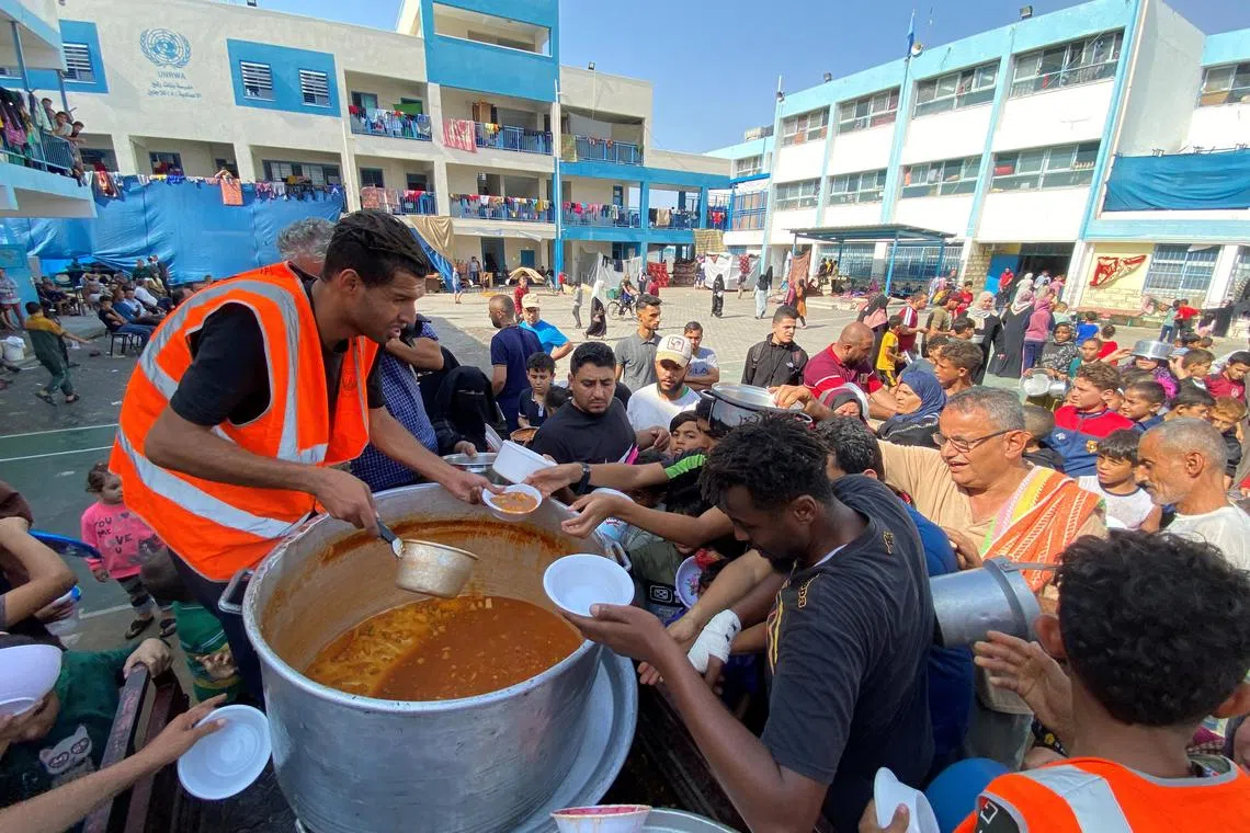 Palestinians, who fled their houses due to Israeli strikes, gather to get their share of charity food offered by volunteers, amid food shortages, at a UN-run school where they take refuge, in Rafah, in the southern Gaza Strip, October 23, 2023. REUTERS/Mahmoud al-Masri