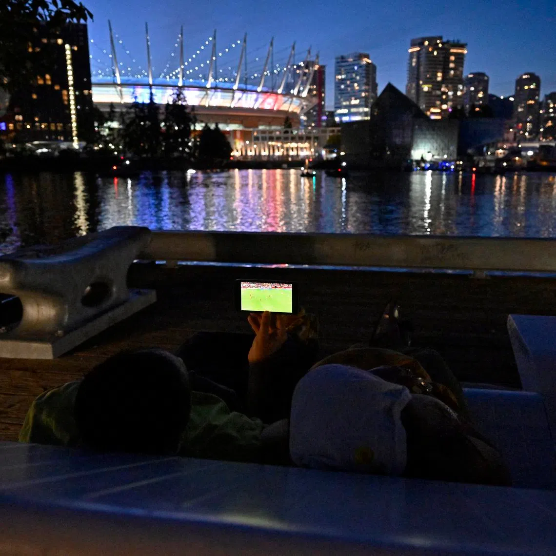 Soccer Football - FIFA World Cup 2026 - Group D - Australia v Turkey - Fans gather in Vancouver - Vancouver, Canada - June 13, 2026 A couple watches the match on their phone near the BC Place stadium REUTERS/Jennifer Gauthier
