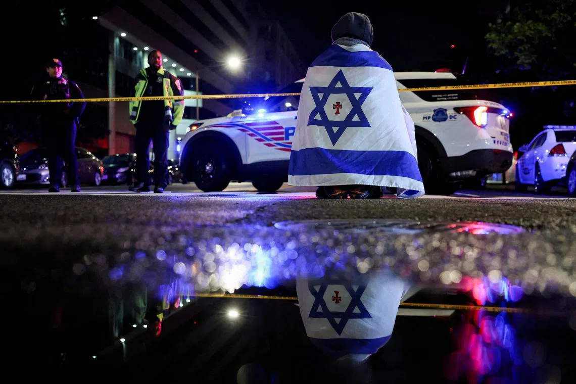 FILE PHOTO: A man, with an Israeli flag with a cross in the center, looks on next to police officers working at the site where, according to the U.S. Homeland Security Secretary, two Israeli embassy staff were shot dead near the Capital Jewish Museum in Washington, D.C., U.S. May 21, 2025.  REUTERS/Jonathan Ernst/File Photo