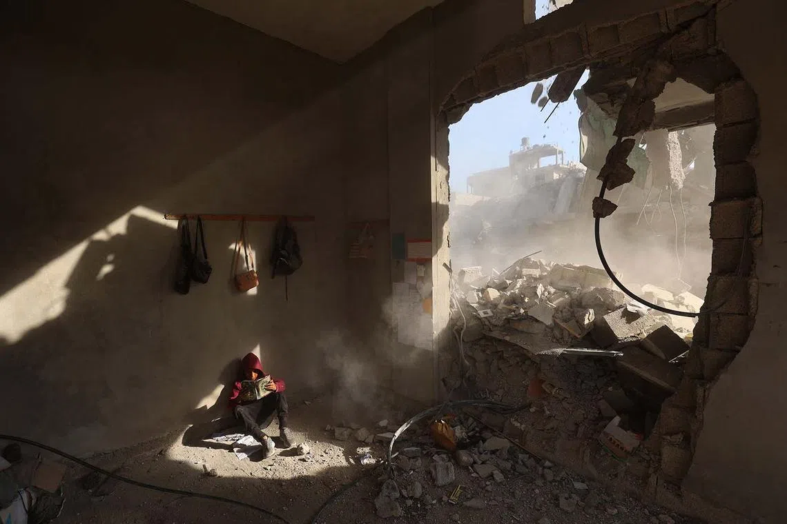 A Palestinian boy holding a book as he sits amongst the rubble of a house, following overnight Israeli strikes, at the Nuseirat refugee camp in the central Gaza Strip on April 29, 2025. 