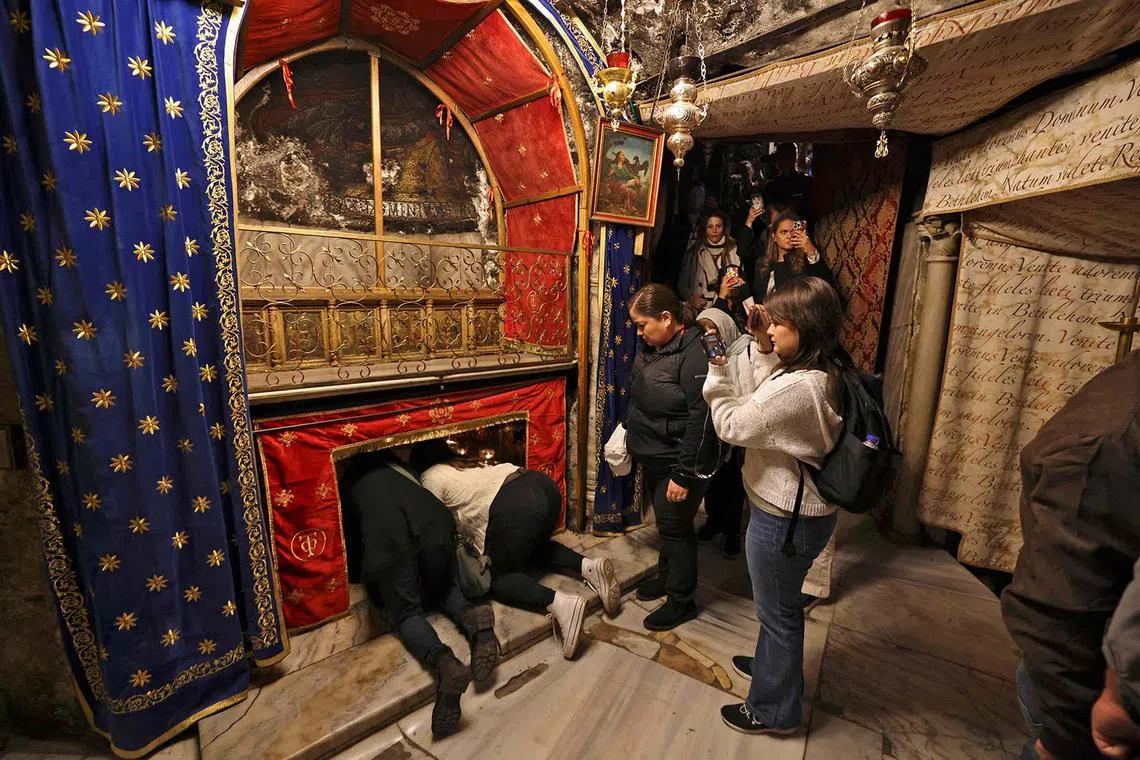 Pilgrims bend to reach for the grotto, believed to be the site of the birth of Jesus, at the Church of the Nativity in the biblical city of Bethlehem in the occupied West Bank during an Advent season visit on December 13, 2022. (Photo by HAZEM BADER / AFP)