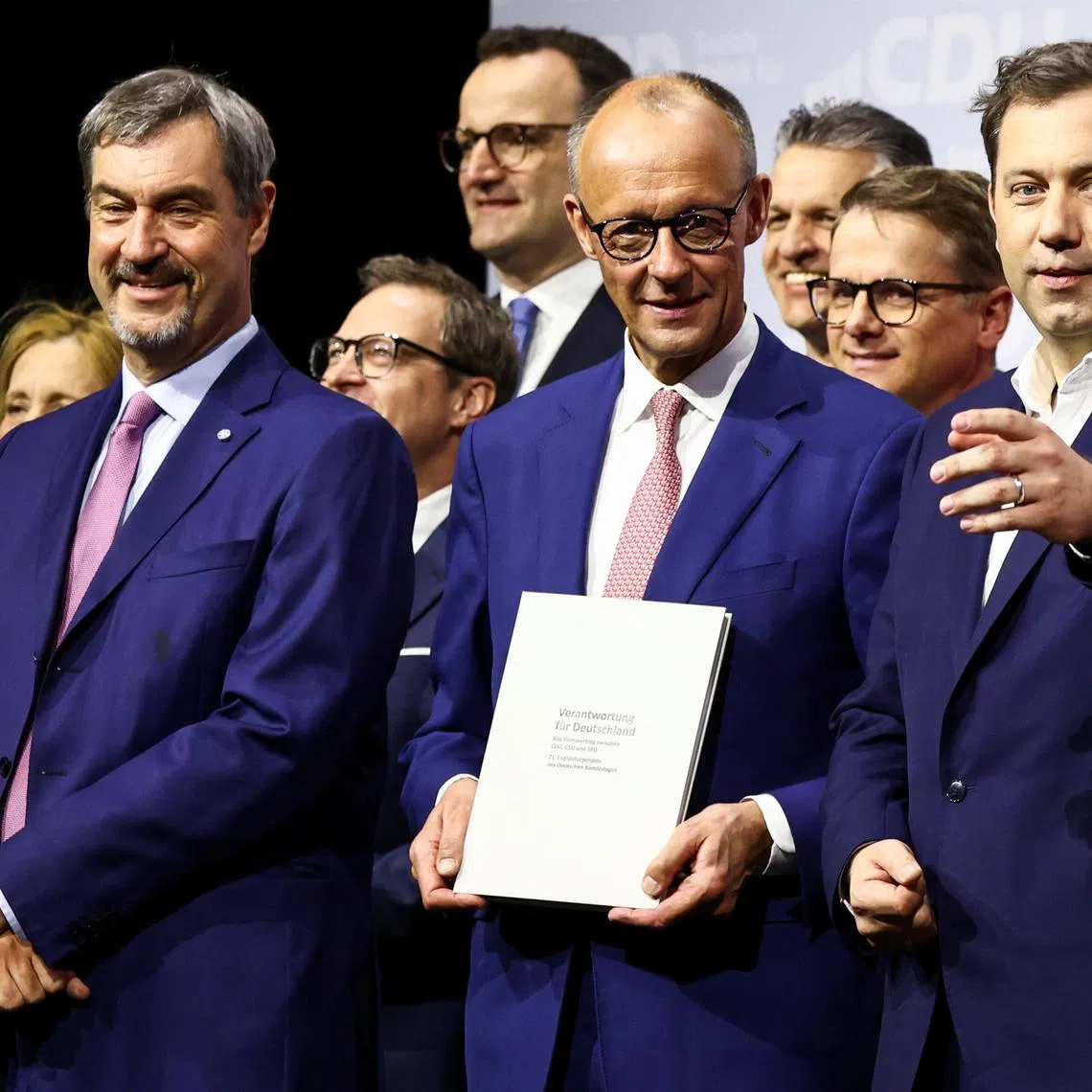 Incoming German Chancellor and leader of the Christian Democratic Union (CDU) Friedrich Merz holds the coalition government agreement between CDU, CSU and SPD, next to Christian Social Union (CSU) leader and Bavarian Premier Markus Soeder and Designated German Vice Chancellor and Designated Finance Minister Lars Klingbeil, at the Gasometer in Berlin, Germany May 5, 2025. REUTERS/Liesa Johannssen