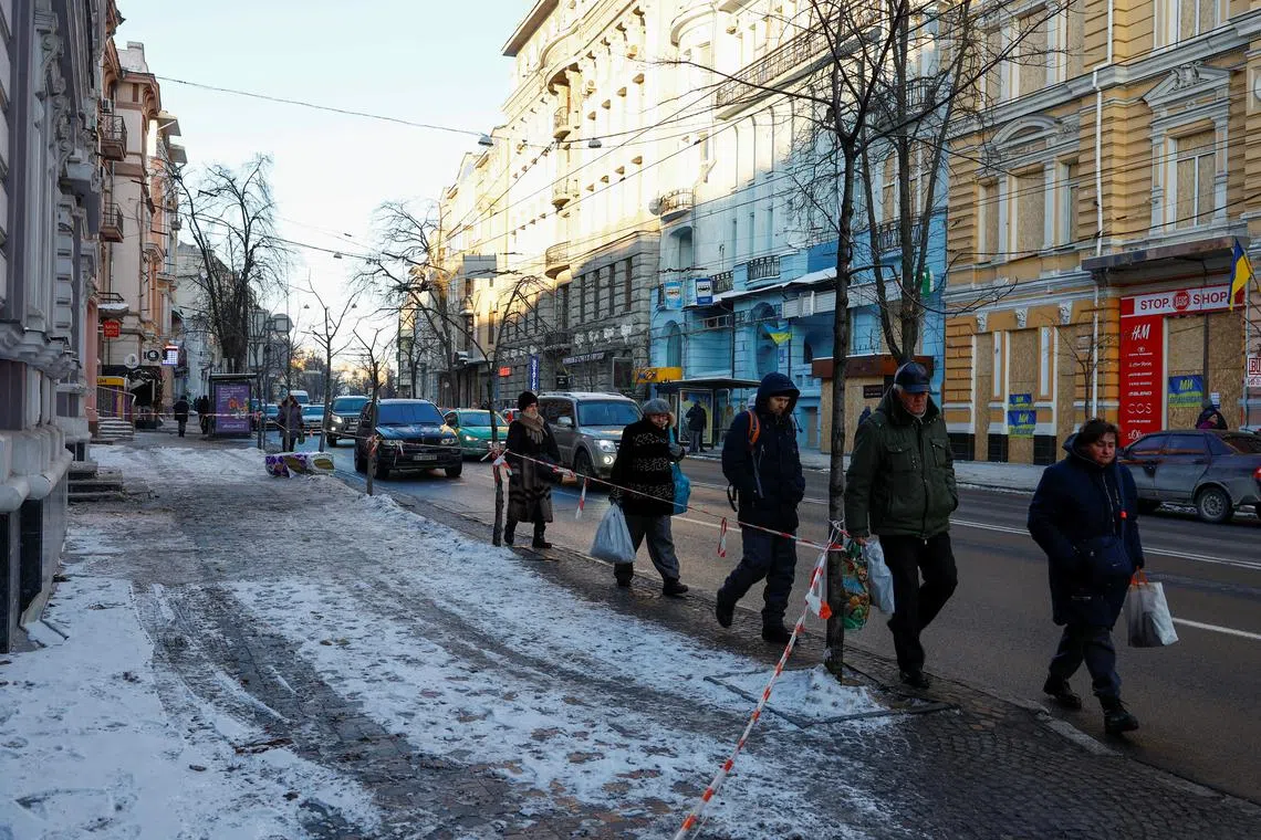 People walk along a street next to historical buildings damaged during one of the latest Russian drone strikes.