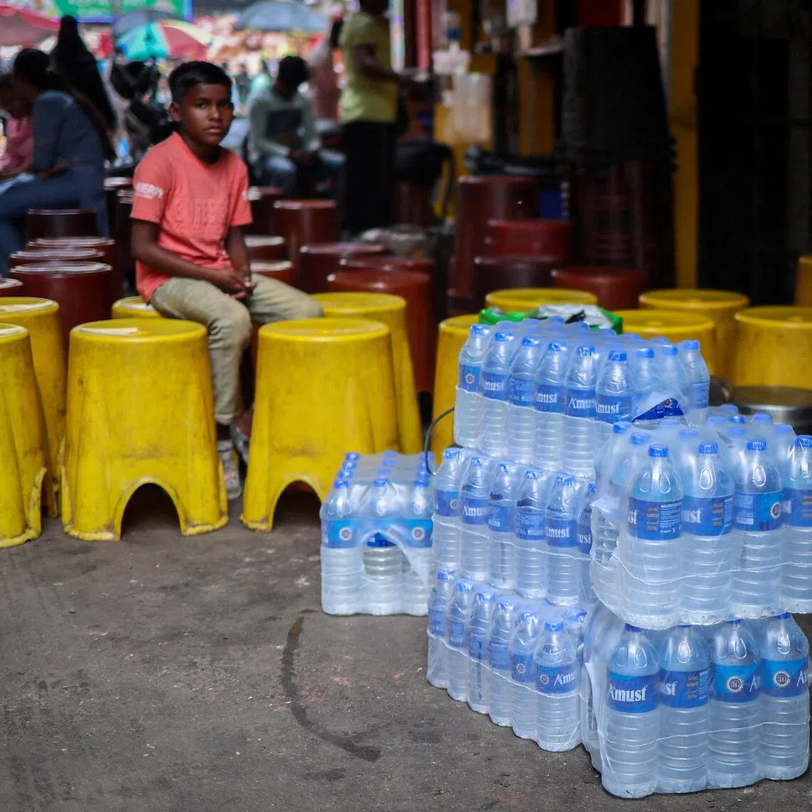 A boy sits next to packed water bottles outside a shop in Kolkata, India on March 12, 2026.
