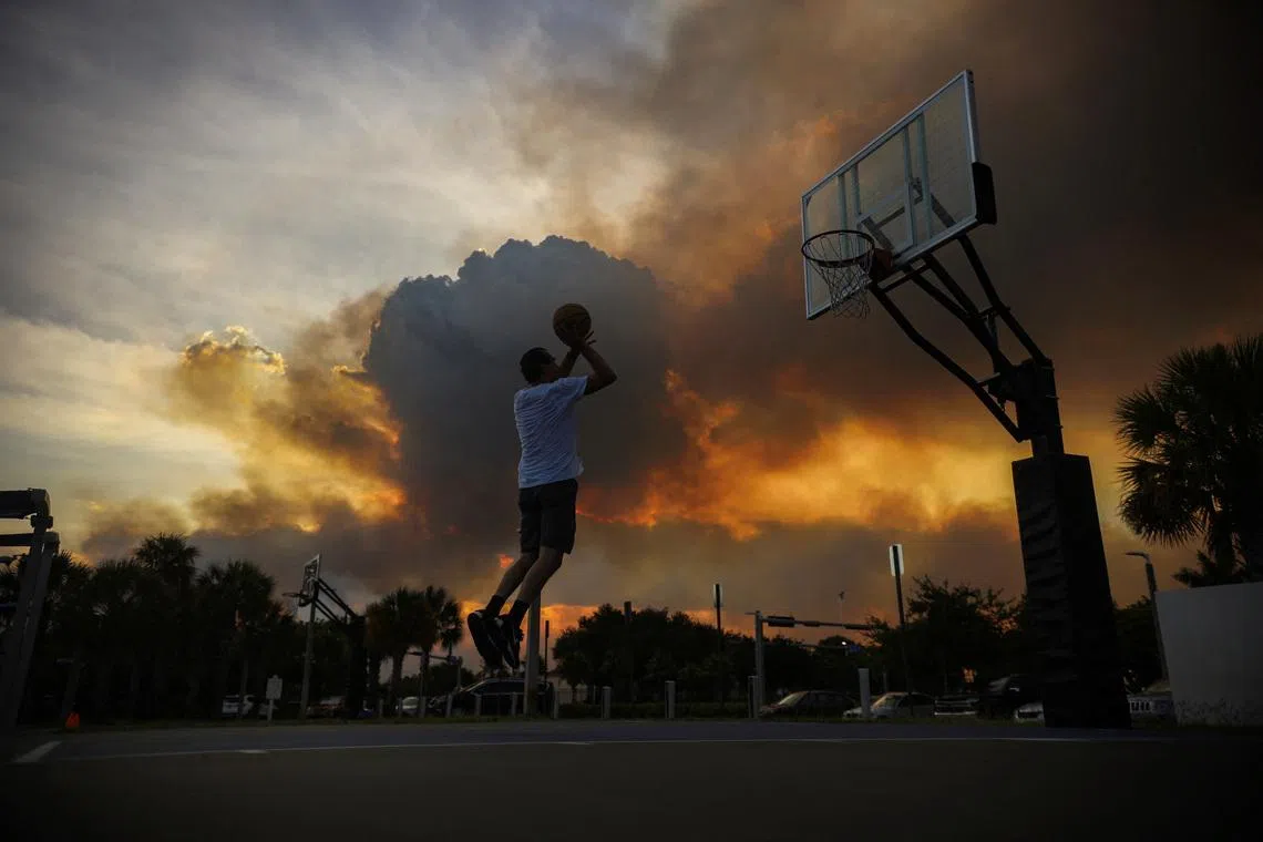 A man playing basketball as a brush fire burns next to the residential neighborhood of Doral in Miami, Florida, US, on June 16, 2026. 