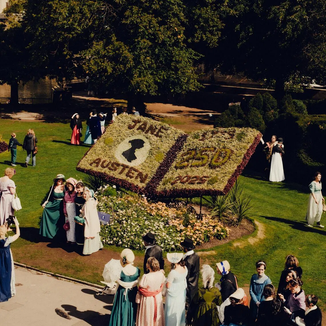 FILE — Costumed attendees take photos with a large flower arrangement during the Grand Regency Costumed Promenade at the annual Jane Austen Festival in Bath, England, on Sept. 12,  2025. To capture the writer’s brief life and enormous impact, we assembled a sampling of the wealth, wonder and weirdness she has brought to our lives. (Peter Flude/The New York Times)
