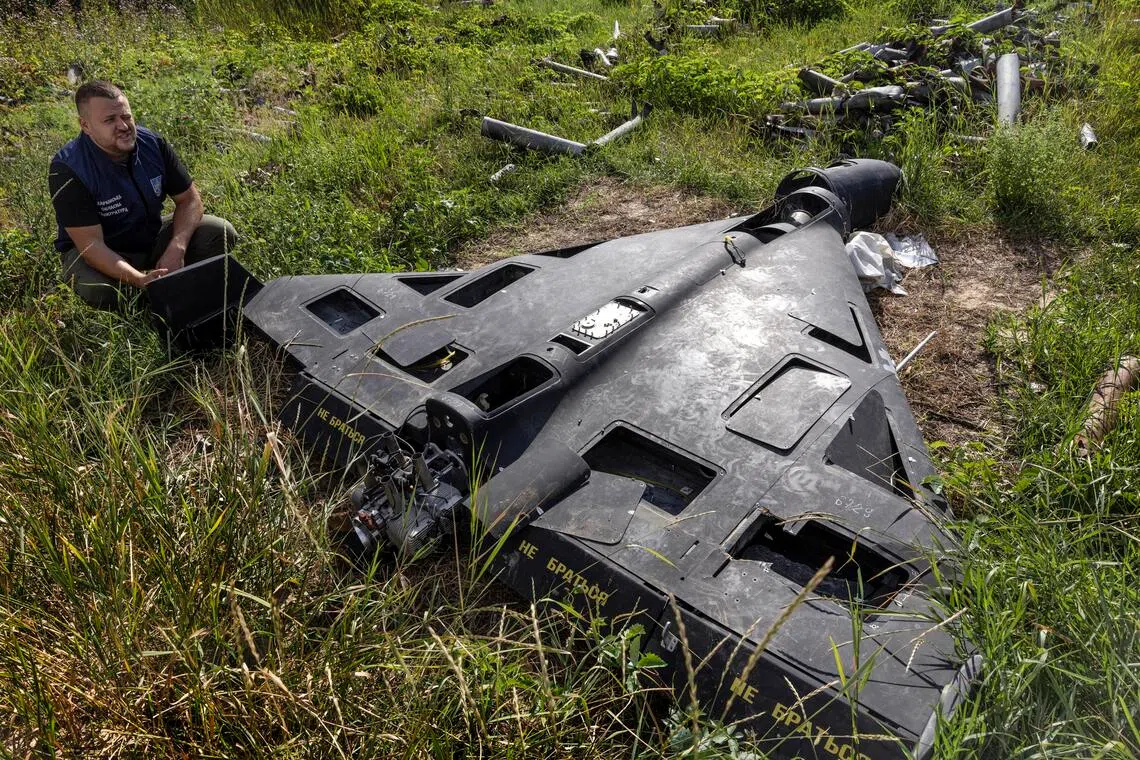 A Ukrainian official kneeling next to a downed Russian drone at a “graveyard” for war ordnance in the Kharkiv region of Ukraine, in July 2025.