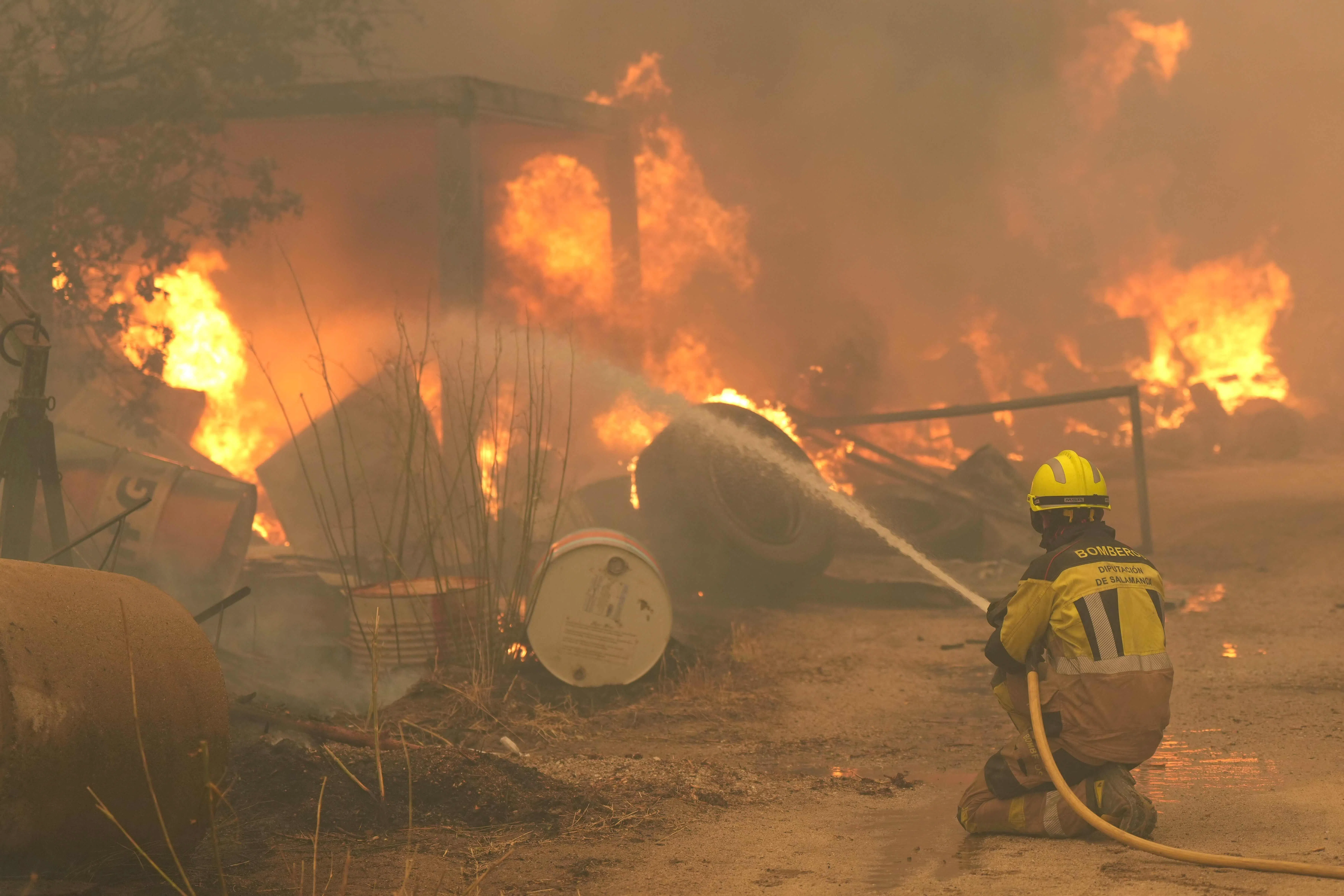 A firefighter waters burning tires and barrels while battling a wildfire in Cebreros area, near Avila, 80 kms west of Madrid on July 24, 2026. The worst wildfires in the Madrid region's history rage west of the Spanish capital, forcing authorities to evacuate or order around 40,000 people to remain indoors. (Photo by Cesar MANSO / AFP)