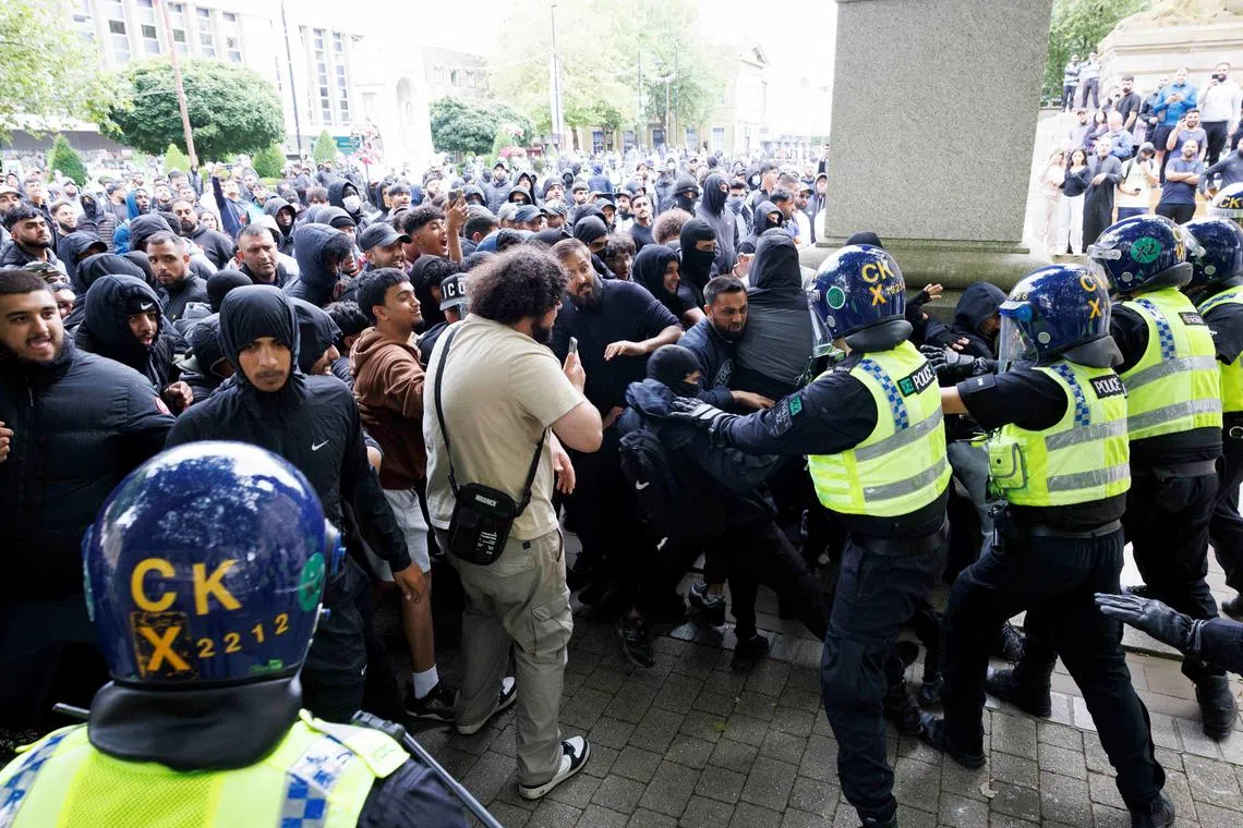 Police officers stand guard as counter-protesters push against the police cordon on the day of a protest against illegal immigration, in Bolton, Britain, August 4, 2024. REUTERS/Belinda Jiao