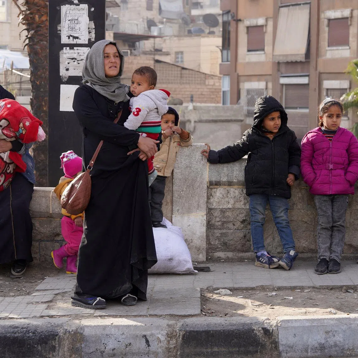 A woman carries her child as she flees, following renewed clashes between the Syrian army and the Syrian Democratic Forces (SDF), in Aleppo, Syria, January 7, 2026. REUTERS/Karam al-Masri