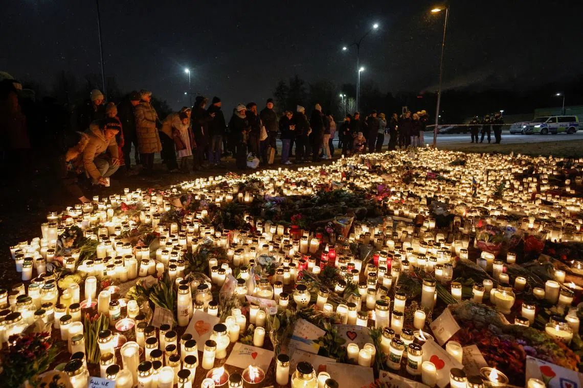 People stand next to candles and flowers placed near the Risbergska school following the deadly shooting.