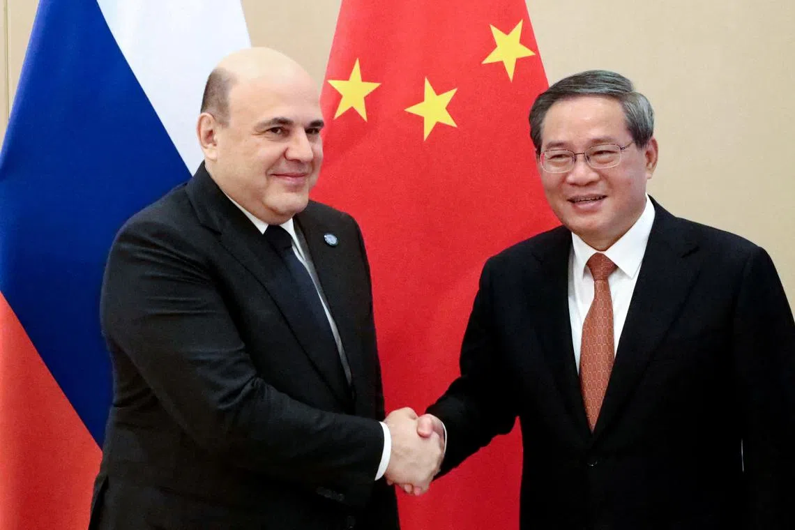 Russian PM Mikhail Mishustin (left) shakes hands with Chinese Premier Li Qiang at the Shanghai Cooperation Organization summit on Oct 16.