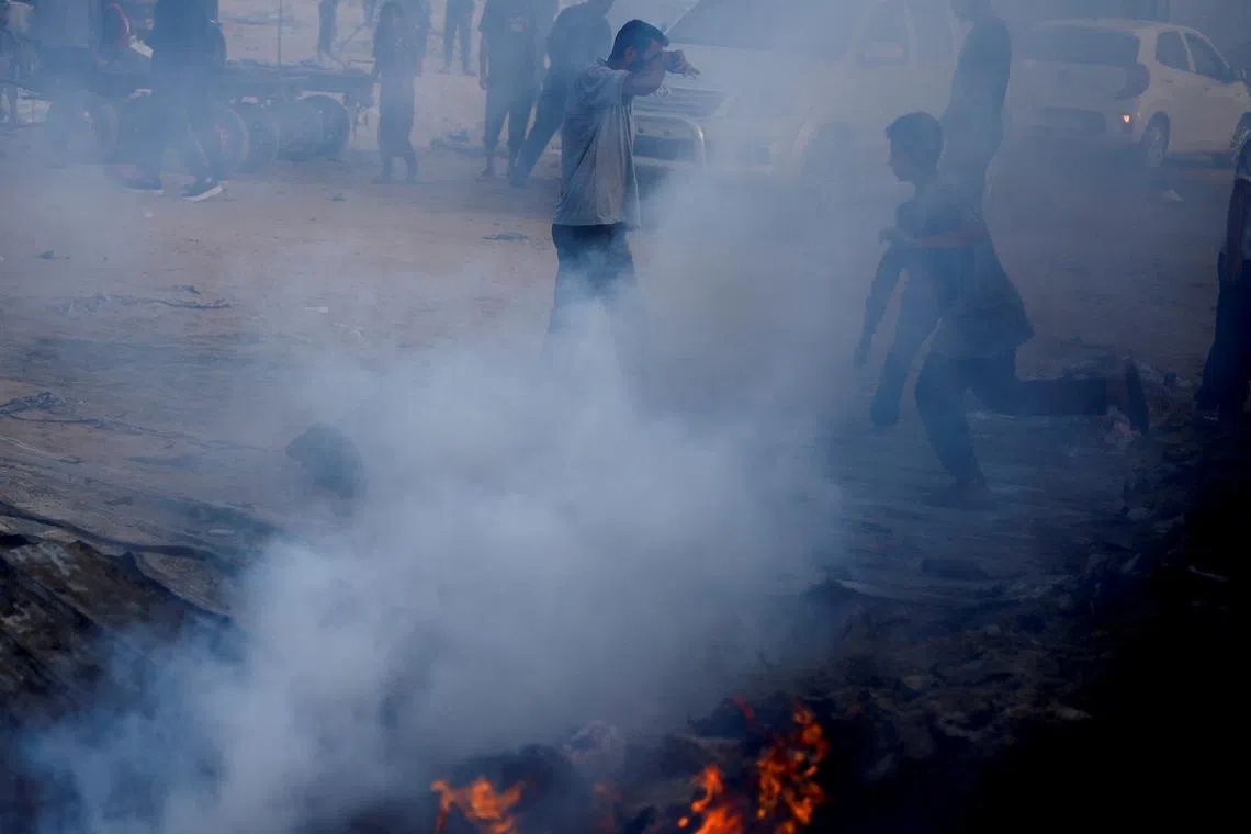 Palestinians walk past smoke rising from a fire at the site of an Israeli strike on an area designated for displaced people, in Rafah, in the southern Gaza Strip, May 27, 2024. REUTERS/Mohammed Salem/ File Photo