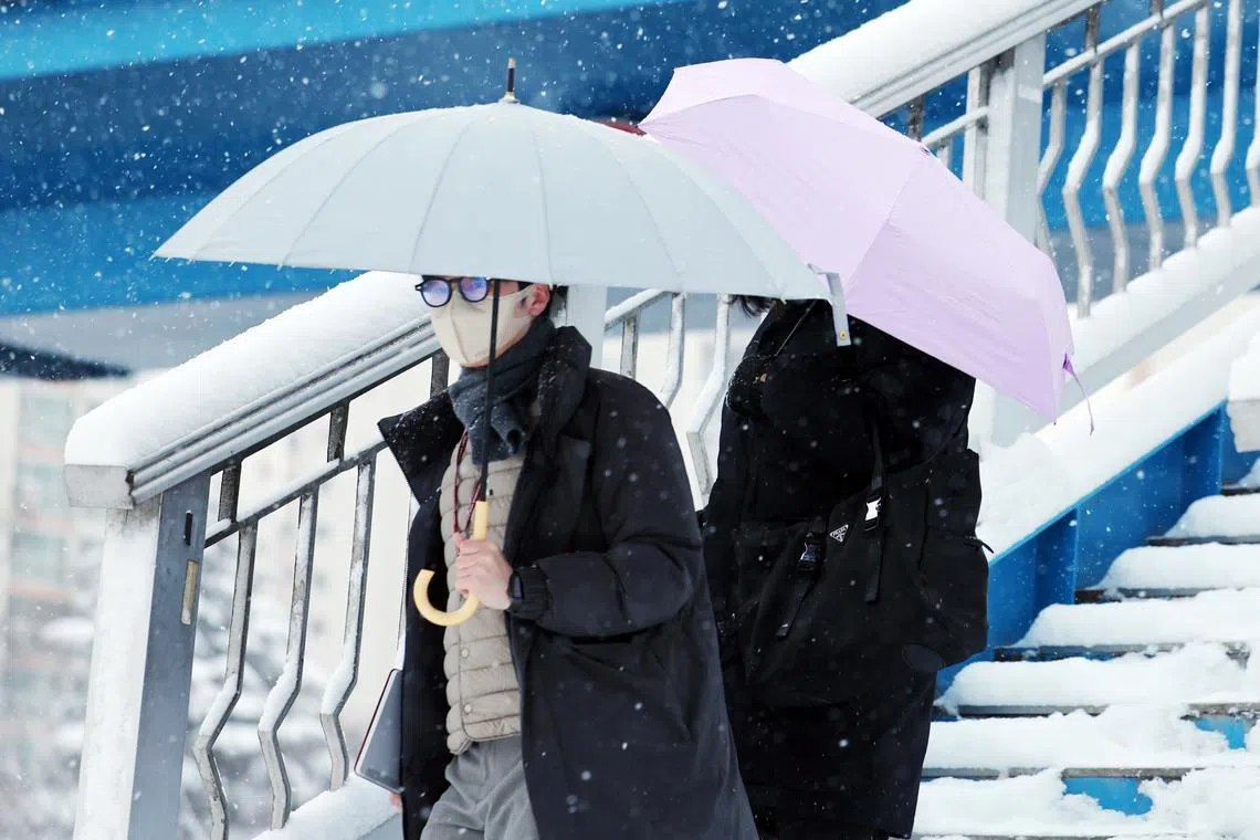 People holding umbrellas walk on a pedestrian overpass during snowfall in Gwangjul, South Korea on Feb 4.