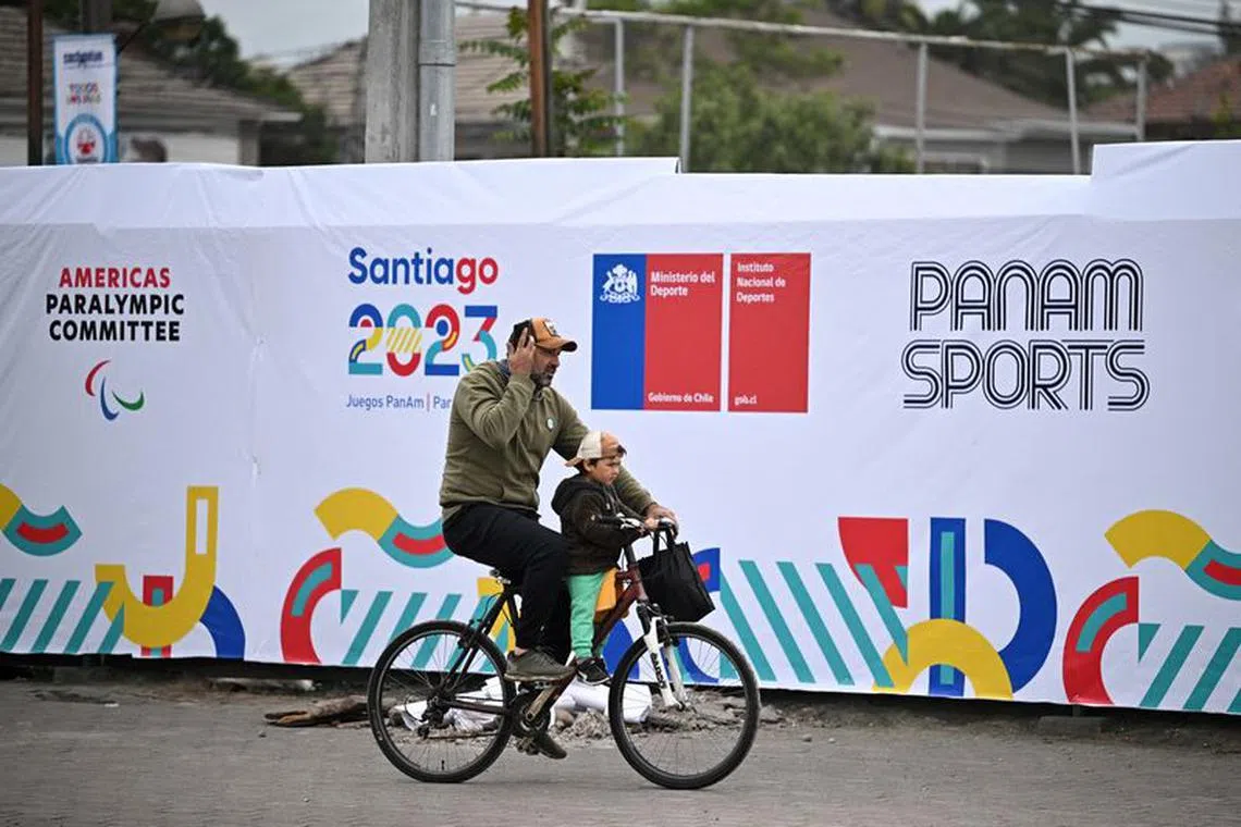 Pan-Am Games - Santiago 2023 - Estadio Nacional, Santiago, Chile - October 20, 2023 A man and child cycle past signage outside the Estadio Nacional ahead of the Pan Am games REUTERS/Dylan Martinez