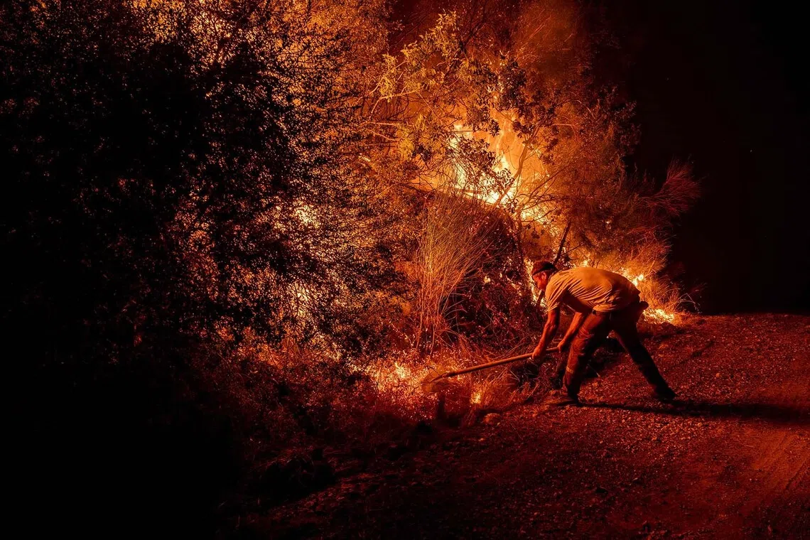 TOPSHOT - A volunteer uses a shovel as they battle a wildfire at Seydikemer district in Mugla on July 29, 2026. Turkish firefighters on July 29, 2026, battled wildfires near the country's southern tourist beaches that have forced the evacuation of hundreds of people, authorities said. Hundreds of firefighters went up against the biggest fire in Mugla province, with more than 20 planes and helicopters bombing water on the flames, the agriculture ministry said. (Photo by Murat Kocabas / AFP)