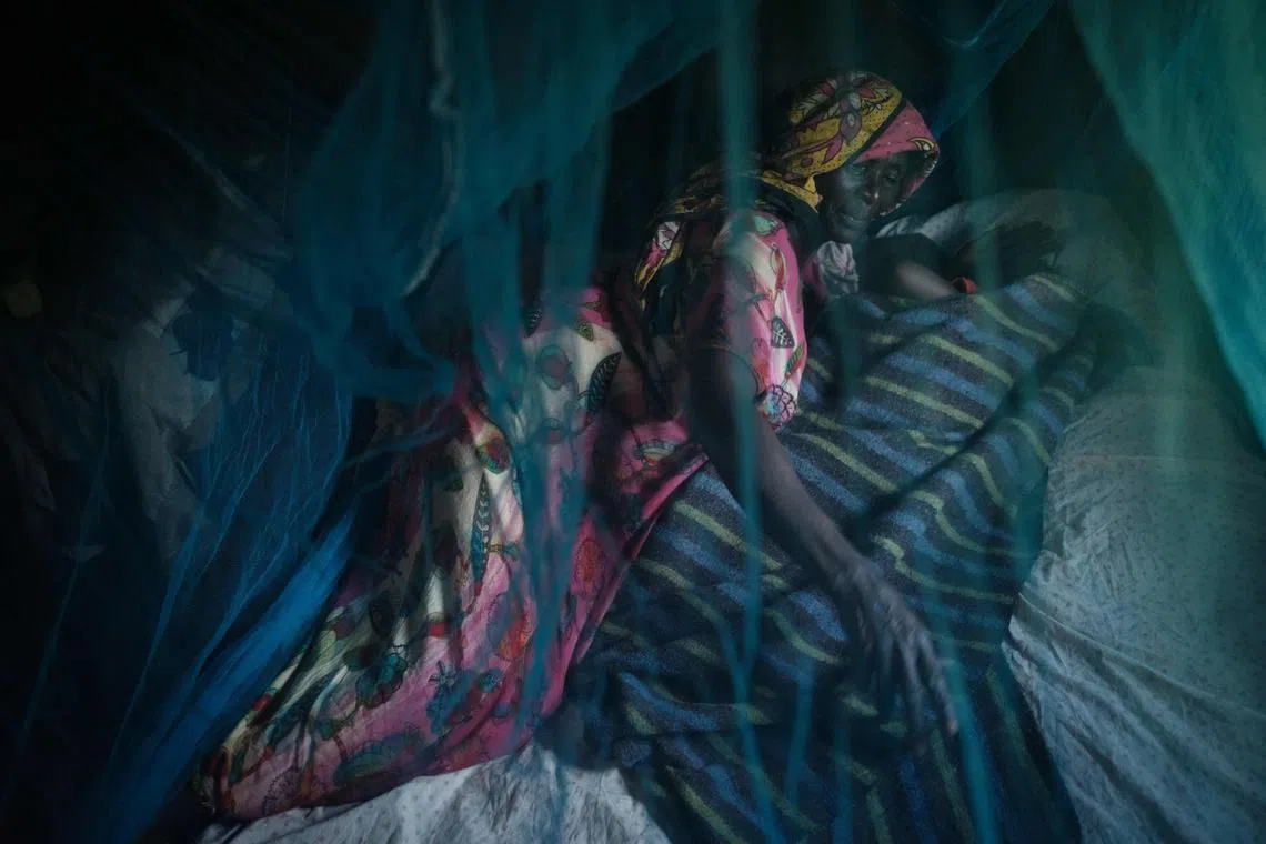 Ruth Kavere (left), 65, demonstrating the use of a mosquito net with her granddaughter Faith, 3, at home in Mukuli, Kenya, on March 7, 2023. The spread of a mosquito in East Africa that thrives in urban areas and is immune to insecticide is fuelling a surge in malaria that could reverse decades of progress against the disease, experts say.