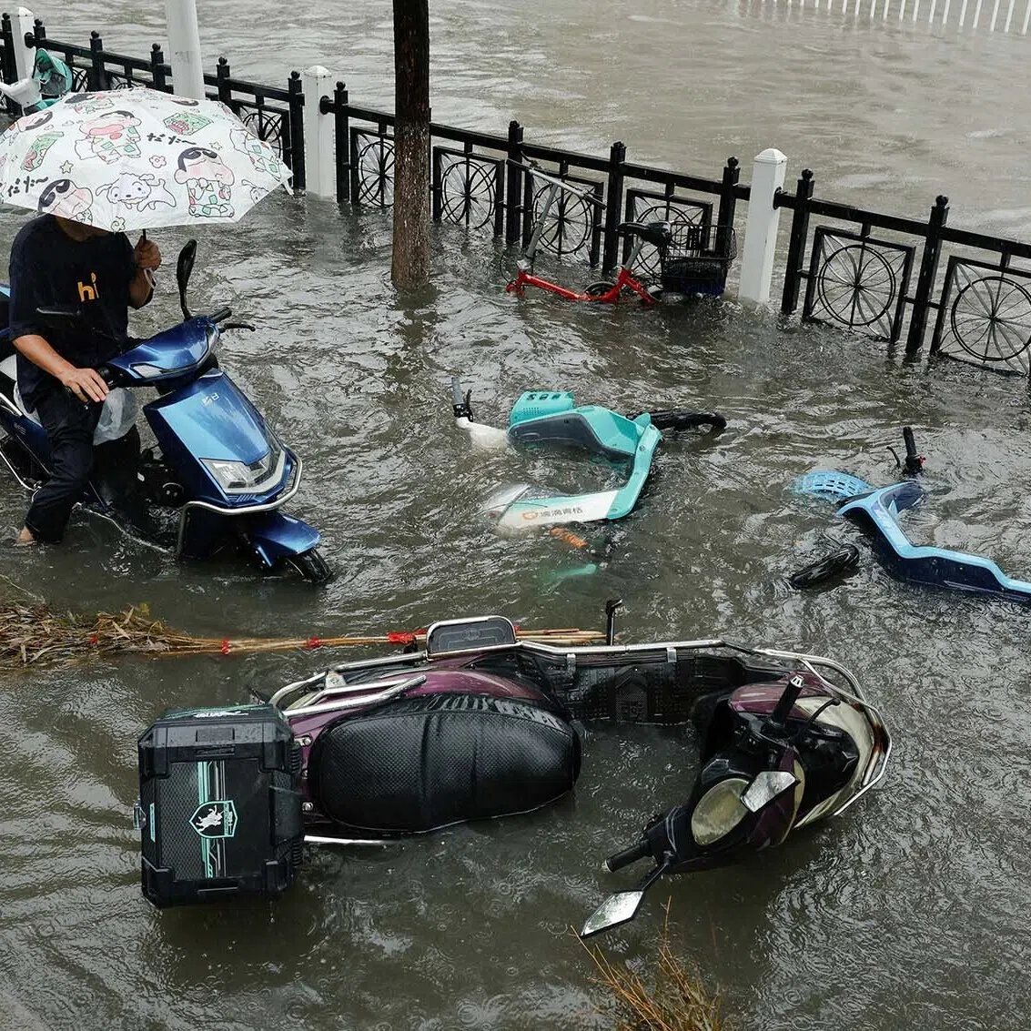 A person rides an electric scooter on a flooded street while avoiding fallen bicycles during heavy rain brought by Typhoon Dolphin after it weakened into a tropical storm, in Xiangyang, Hubei province, China, August 11, 2026. REUTERS/Go Nakamura TPX IMAGES OF THE DAY