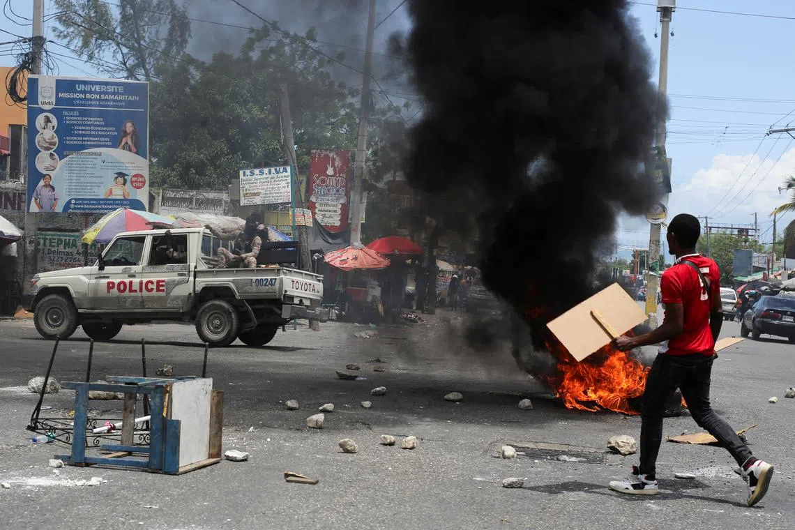FILE PHOTO: A man holds placards as he yells toward a patrol car near a burning barricade during a protest against gang-related violence and to demand the resignation of Haiti's transitional presidential council, in Port-au-Prince, Haiti, May 15, 2025. REUTERS/Jean Feguens Regala/File Photo