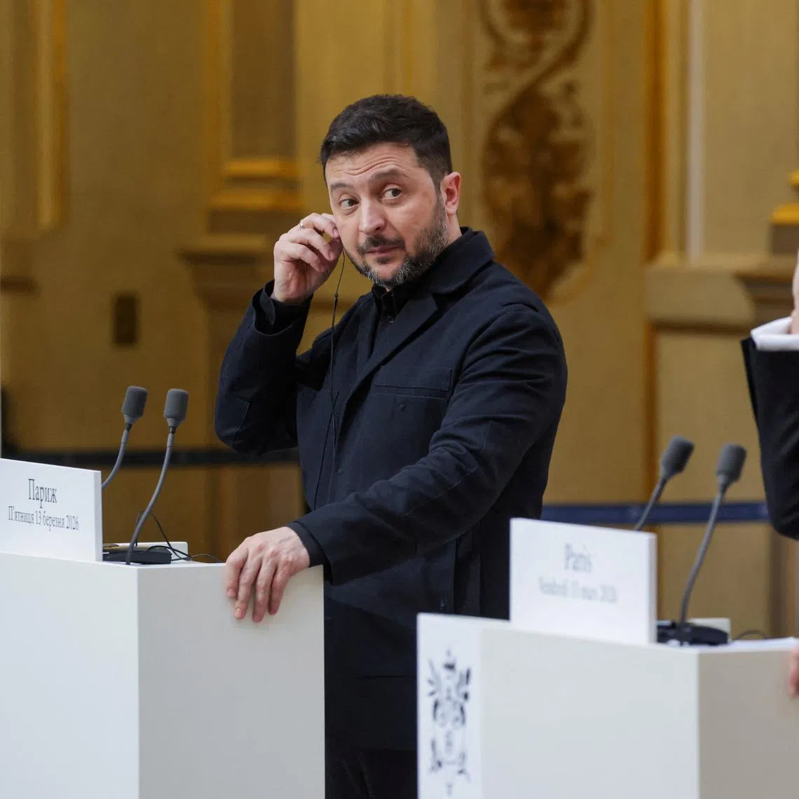Ukraine's President Volodymyr Zelensky (L) and France's President Emmanuel Macron (R) put on a earpiece as they deliver a speech during a joint press conference, in Paris, March 13, 2026.  LUDOVIC MARIN/Pool via REUTERS