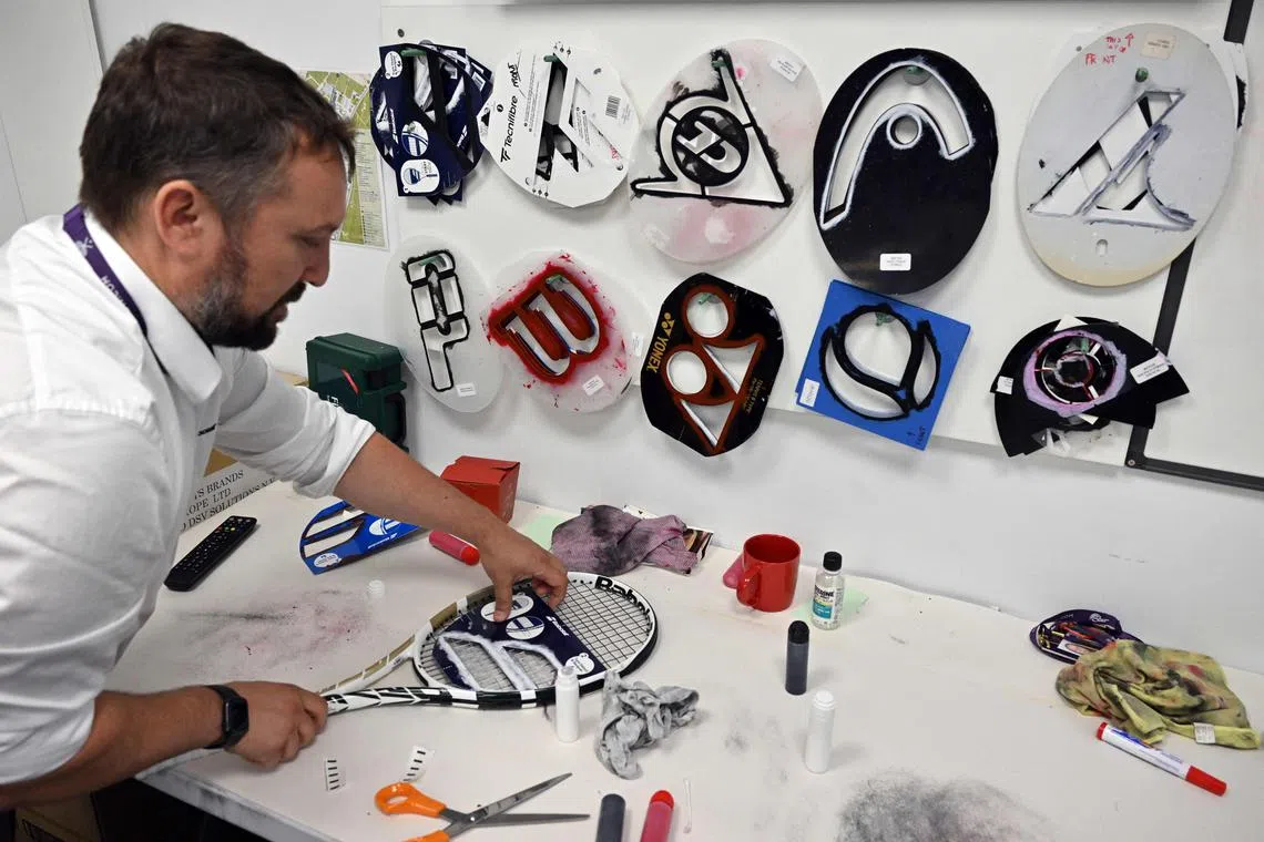 A member of the racquet stringing department stencils a logo on a newly restrung racquet, on the seventh day of the 2023 Wimbledon Championships at The All England Tennis Club in Wimbledon, southwest London on July 9, 2023. 