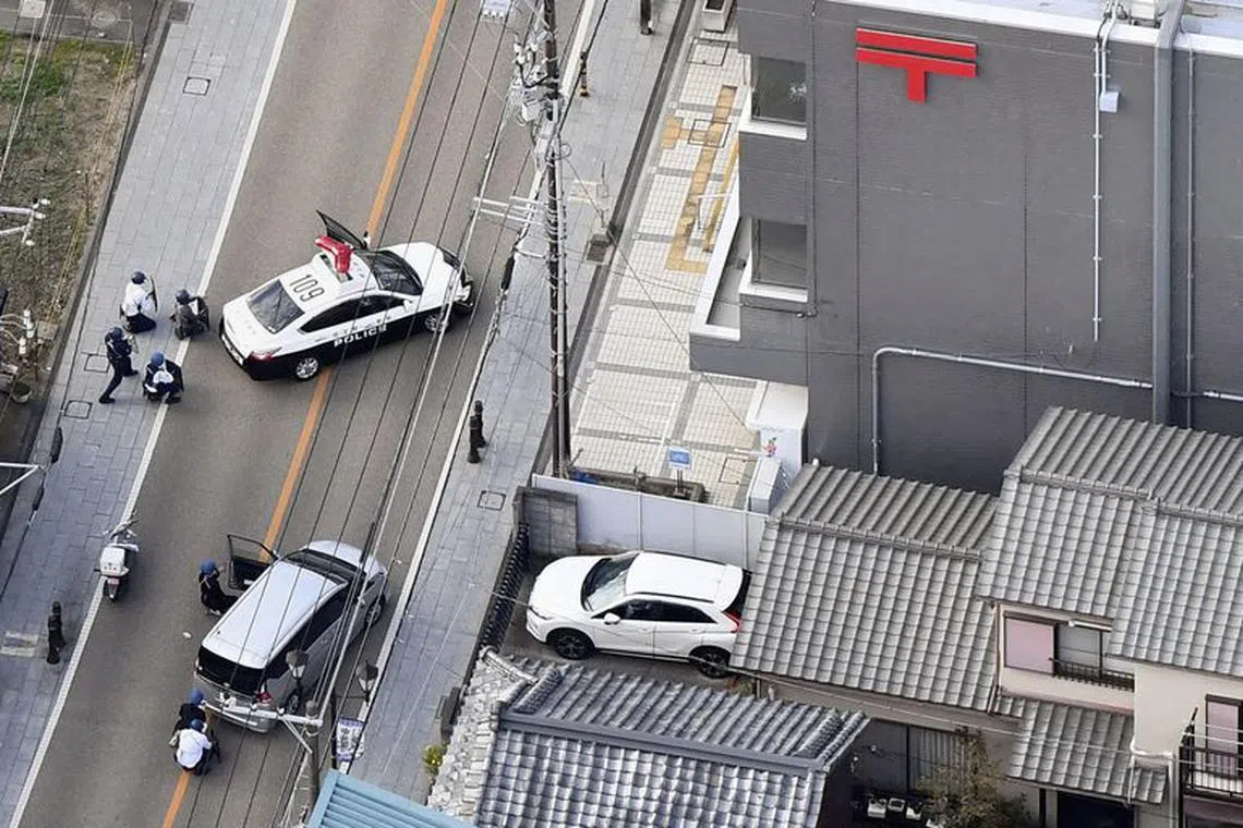 Police officers take cover behind cars outside the post office where a suspected gunman has taken people hostage after injuring two at a hospital, in Warabi, Saitama Prefecture, Japan October 31, 2023, in this photo taken by Kyodo. Mandatory credit Kyodo/via REUTERS
