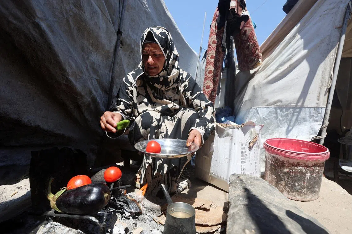 Displaced Palestinian woman Nisreen Abu Saada cook vegetables over a wood fire outside her tent, amid shortages of lighters and cooking gas, in Khan Younis, in the southern Gaza Strip, July 21, 2026. REUTERS/Ramadan Abed